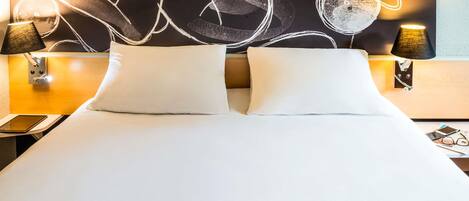 A hotel room with a large bed, two bedside lamps, and a wall with abstract art.
