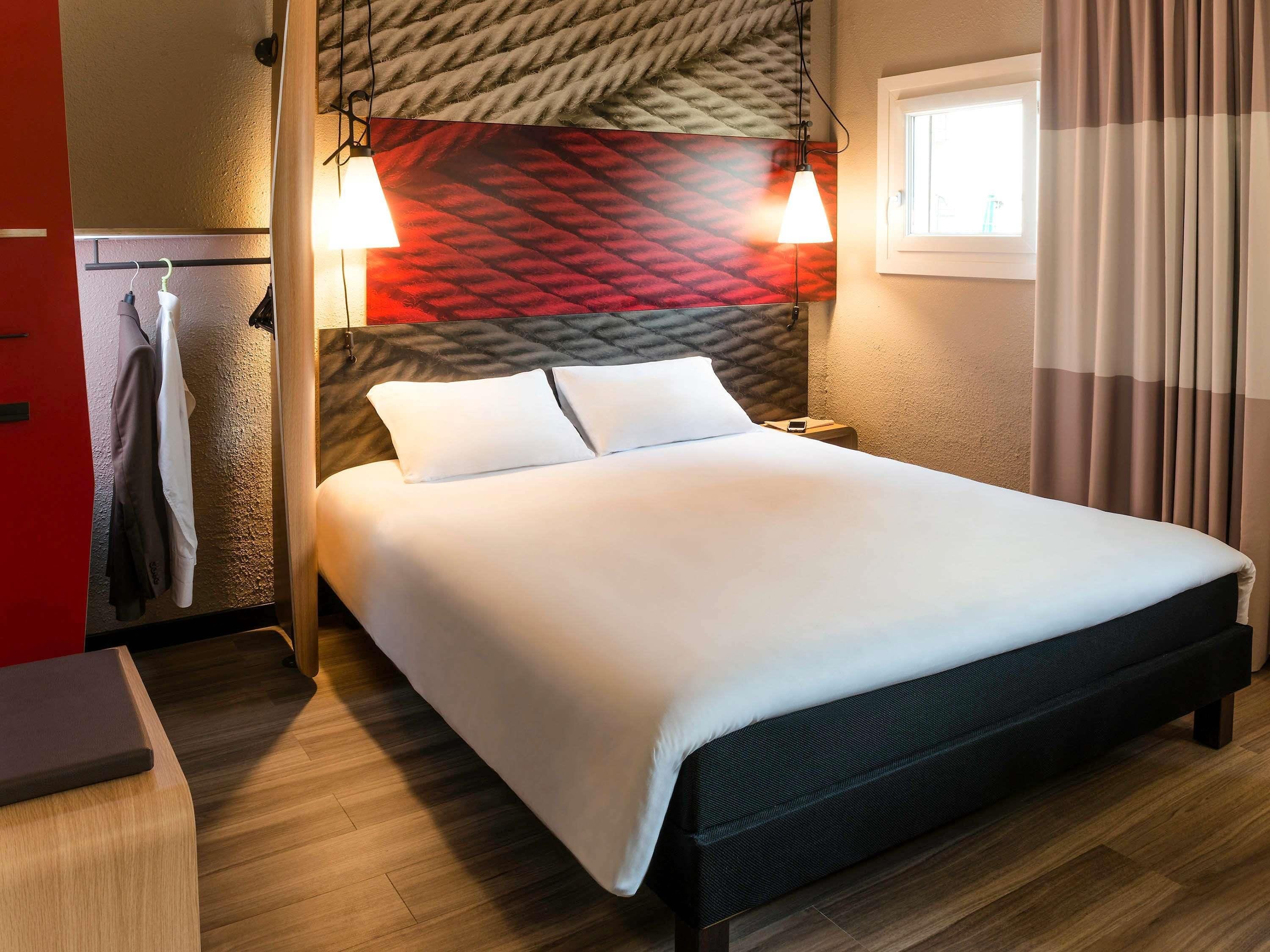 A hotel room with a bed, bedside table, and a wall-mounted lamp.