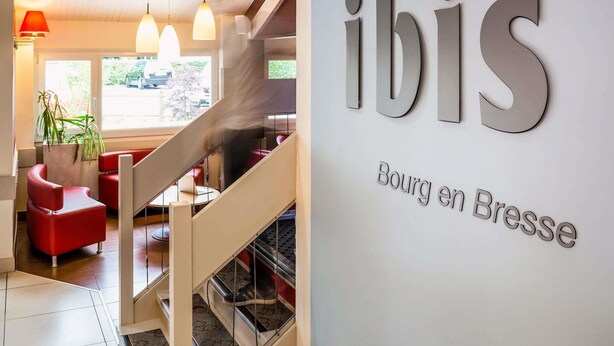 Ein modernes Interieur mit einer Treppe, roten Sitzgelegenheiten und einem Schild mit der Aufschrift 'ibis Bourg en Bresse'.