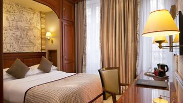 A hotel room with a bed, a desk with a laptop, a chair, a coffee maker, and curtains.