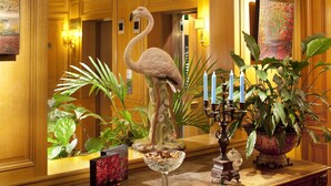 A lobby with a wooden reception desk, a flamingo statue, potted plants, and a painting on the wall. - Hôtel Horset Opéra, BW Premier Collection (Paris)