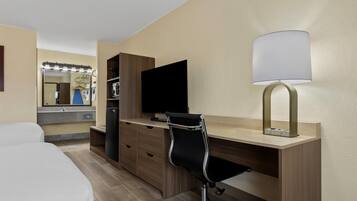 Une chambre d’hôtel comprenant un lit, un bureau avec un ordinateur, une lampe, une télévision, un miroir et une armoire.