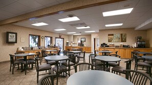A spacious indoor dining area with multiple tables and chairs, a counter with a coffee machine, and framed artwork on the walls.