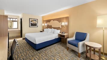 Habitación de hotel con cama, una silla, escritorio, lámpara y espejo.