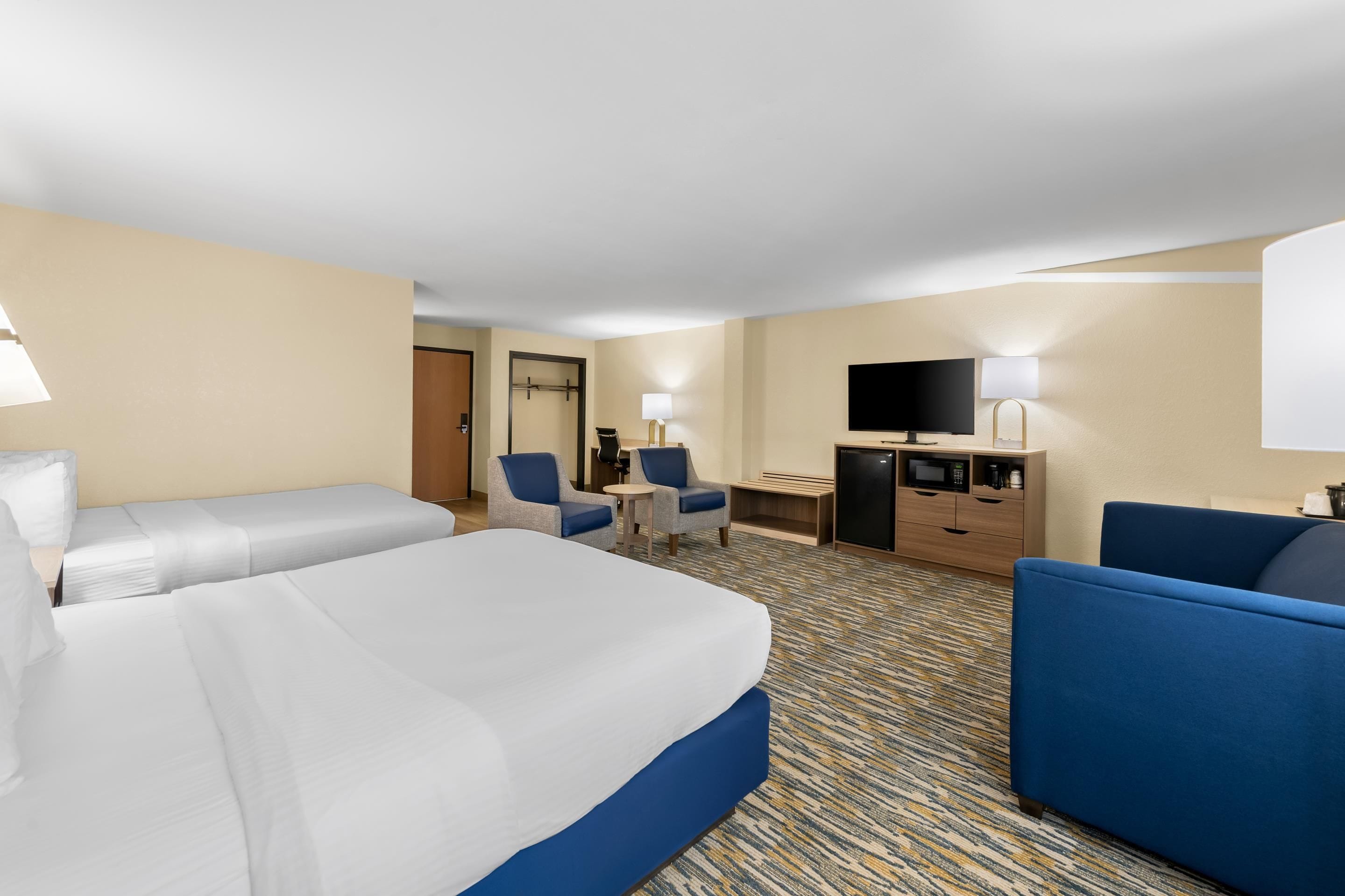 A hotel room with a bed, two chairs, a desk, a television, and a minibar.