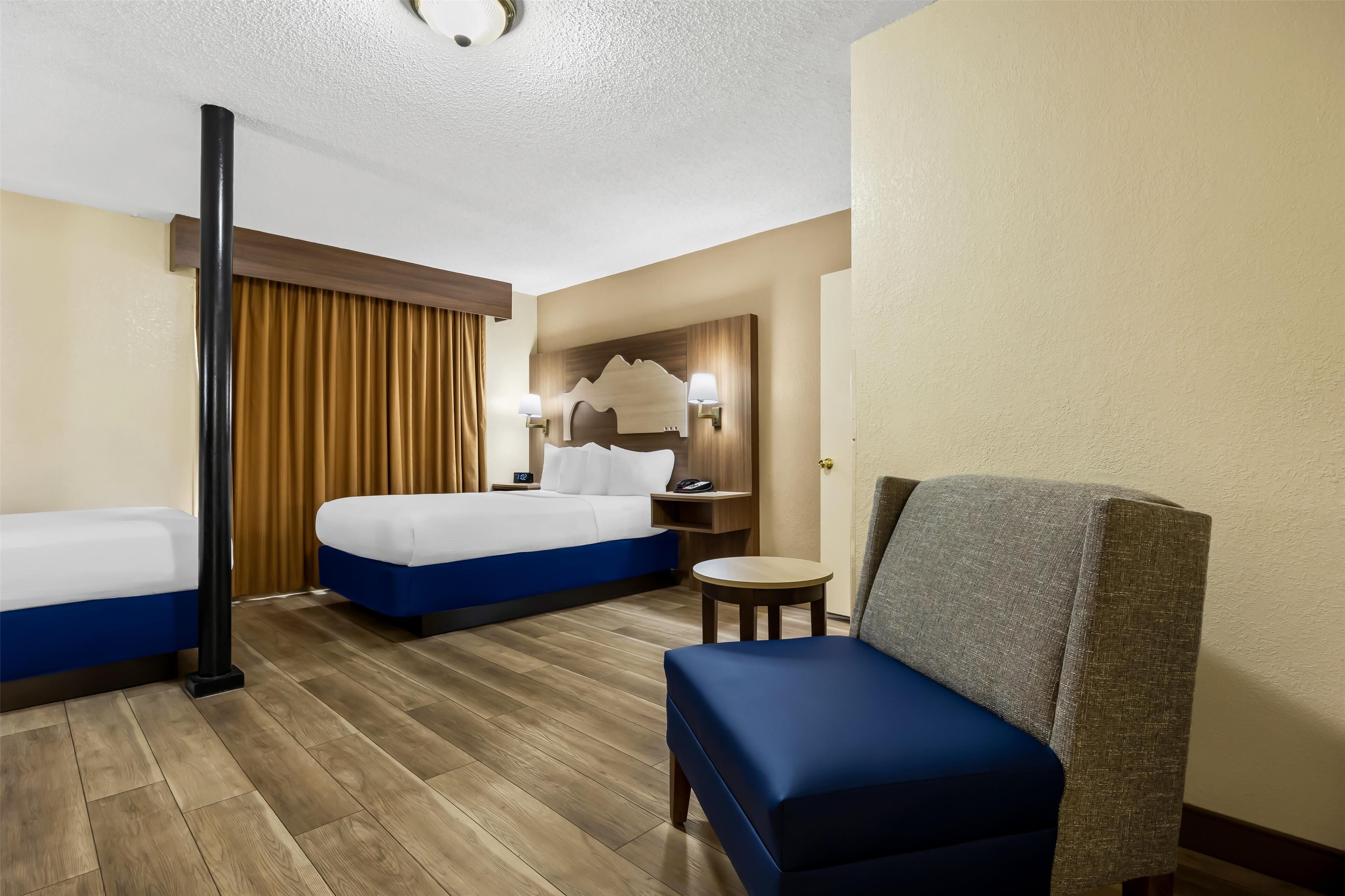 A hotel room with two beds, a chair, a small table, and a wall-mounted TV.