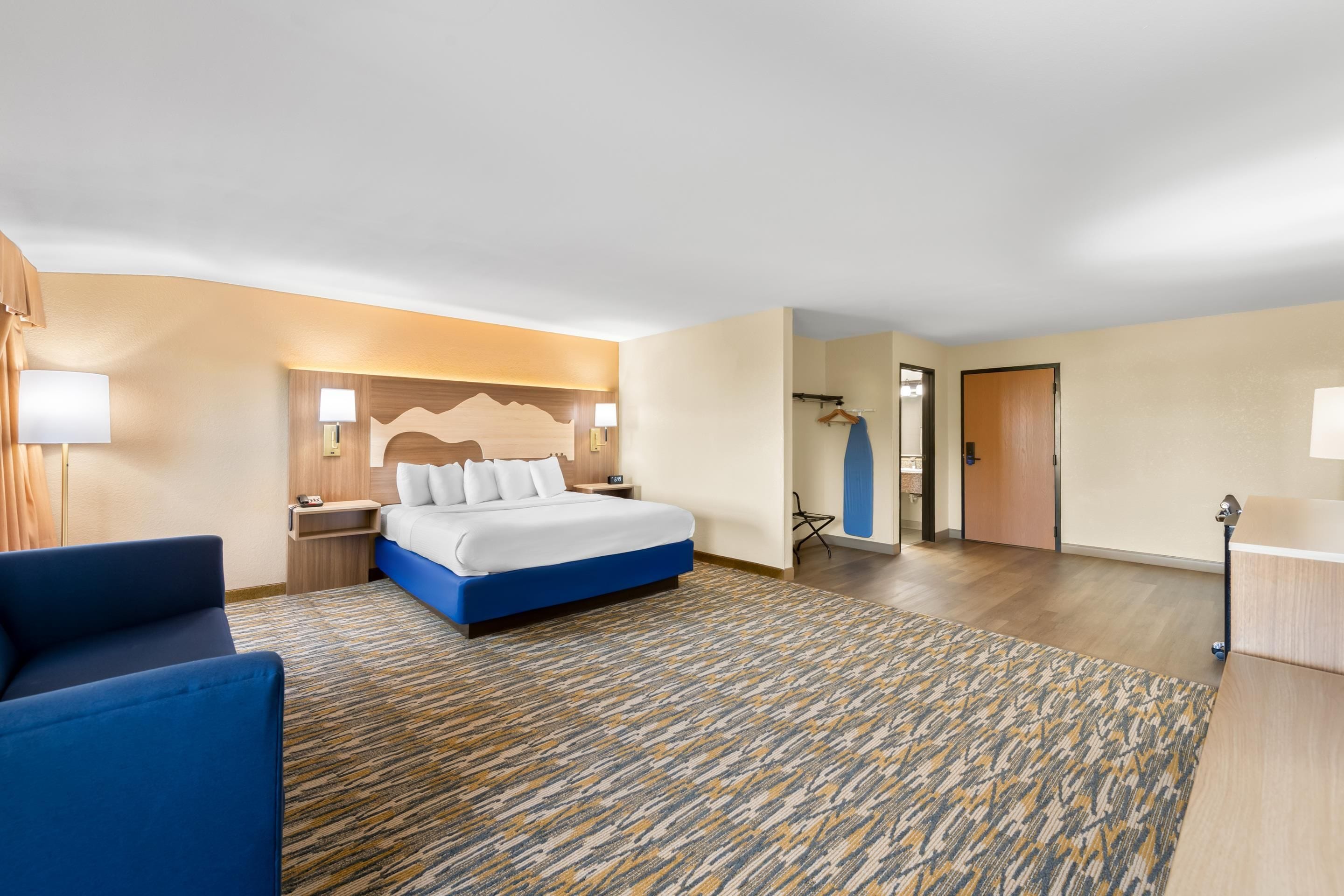 A hotel room with a bed, bedside tables, a desk, a chair, and a patterned carpet.