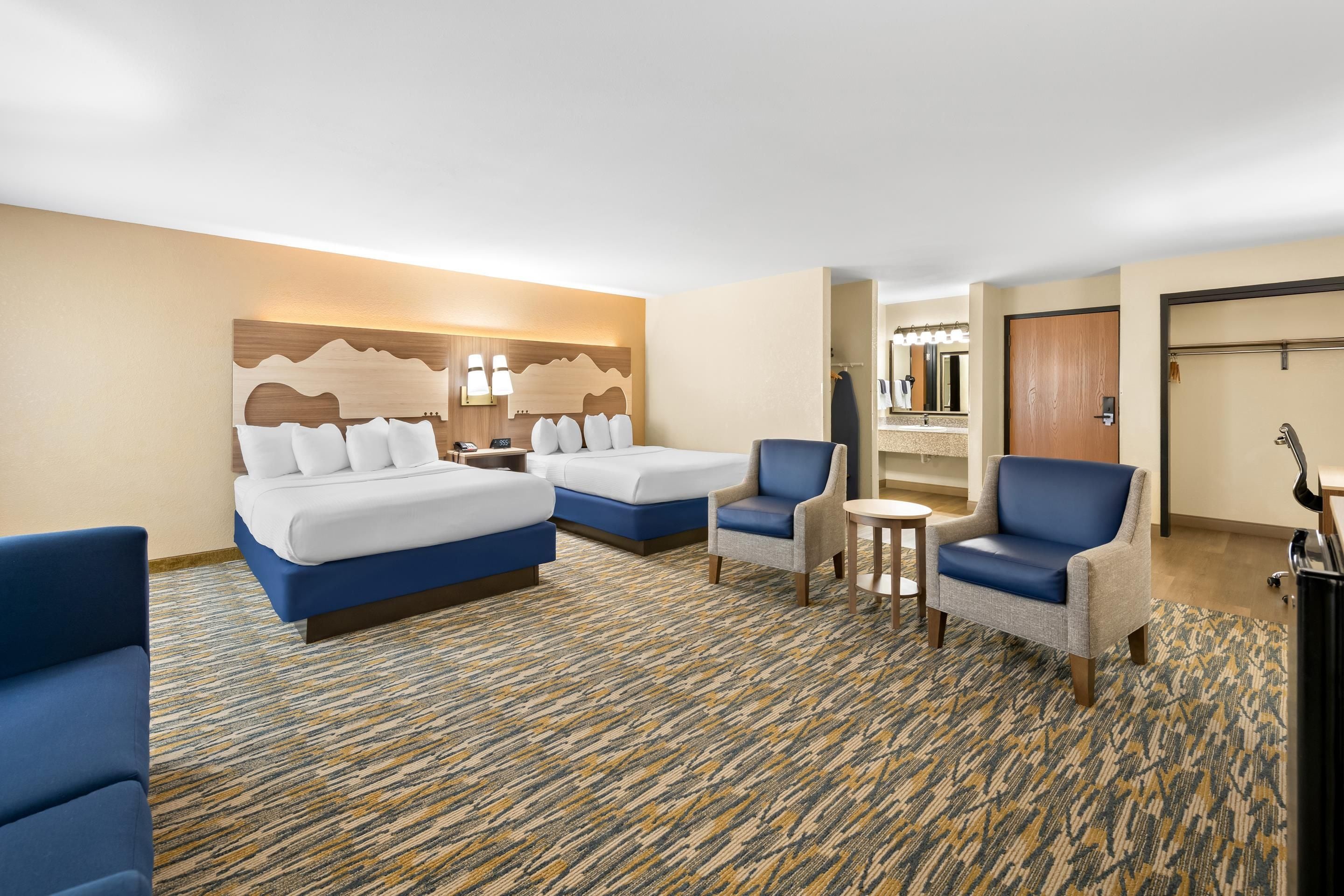 A hotel room with two beds, a seating area with chairs, a small table, and a bathroom visible through an open door.