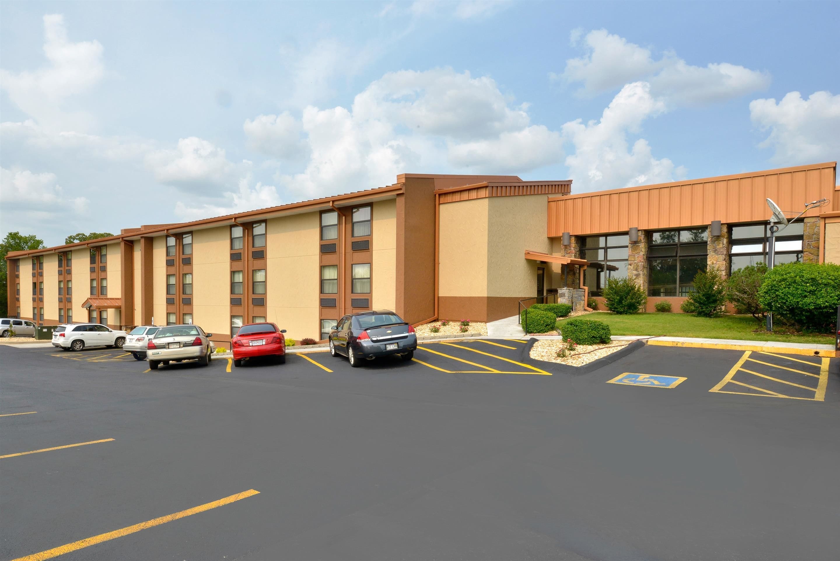 A hotel with a parking lot, multiple cars, and a building with a beige and brown facade.