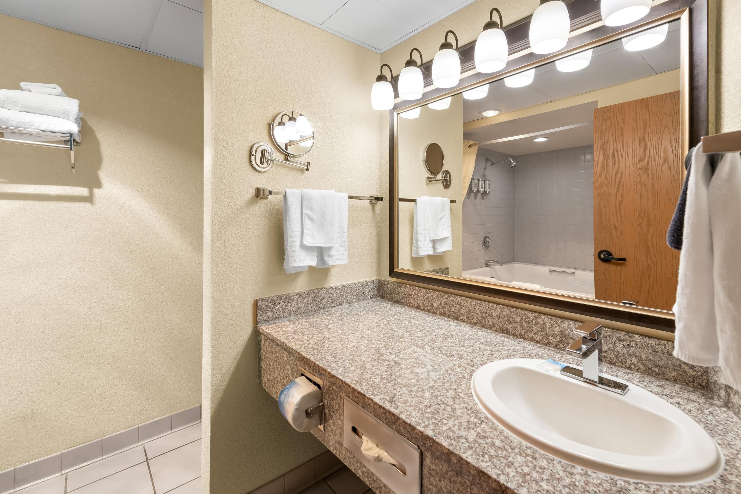 A bathroom with a granite countertop, a sink, a mirror with lights, and a towel rack.
