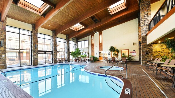 An indoor swimming pool with stone pillars, wooden beams, and a sunlit interior.