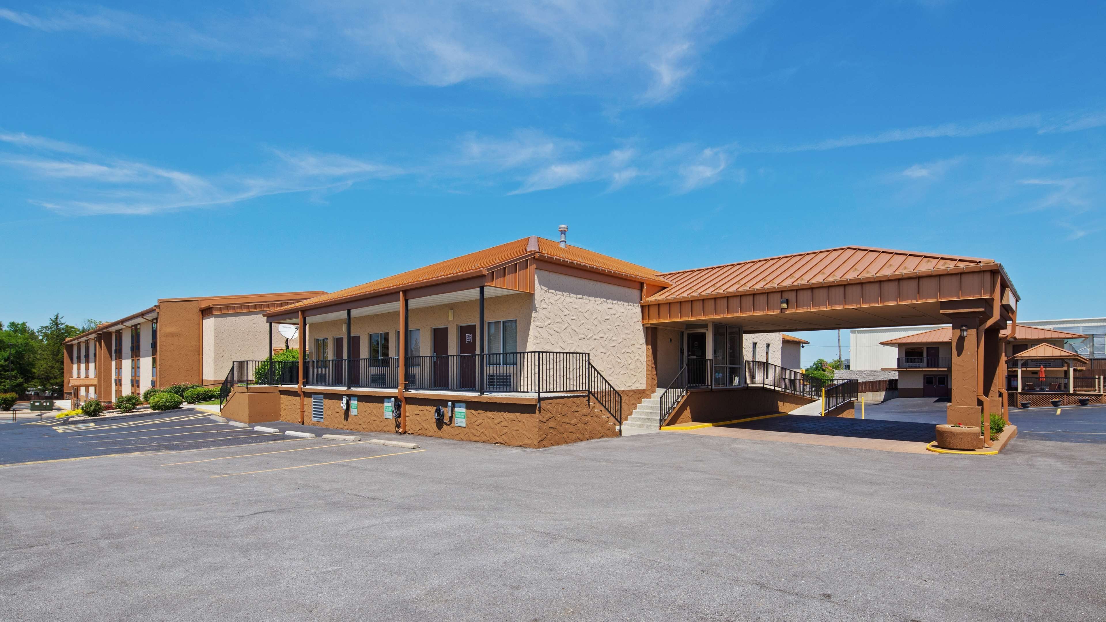 Un motel doté d’un espace extérieur abrité avec des sièges, d’un parking et d’un bâtiment à la façade marron.