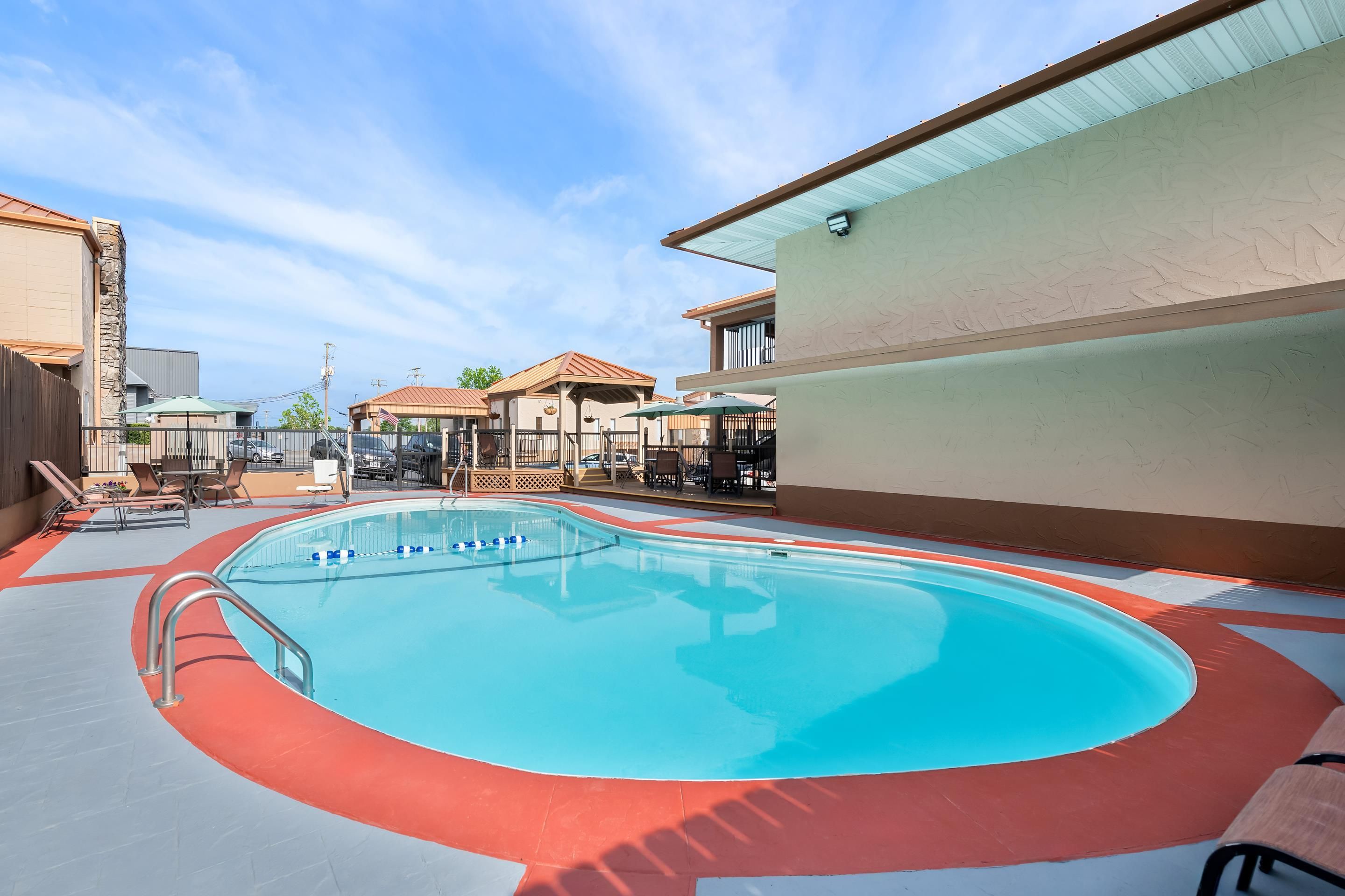 An outdoor swimming pool with a red and blue tiled deck, surrounded by lounge chairs and umbrellas.