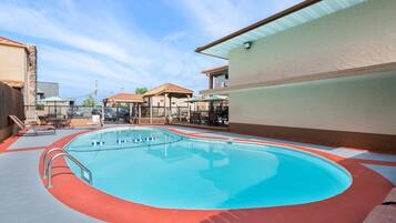 An outdoor swimming pool with a red and blue tiled deck, surrounded by lounge chairs and umbrellas.