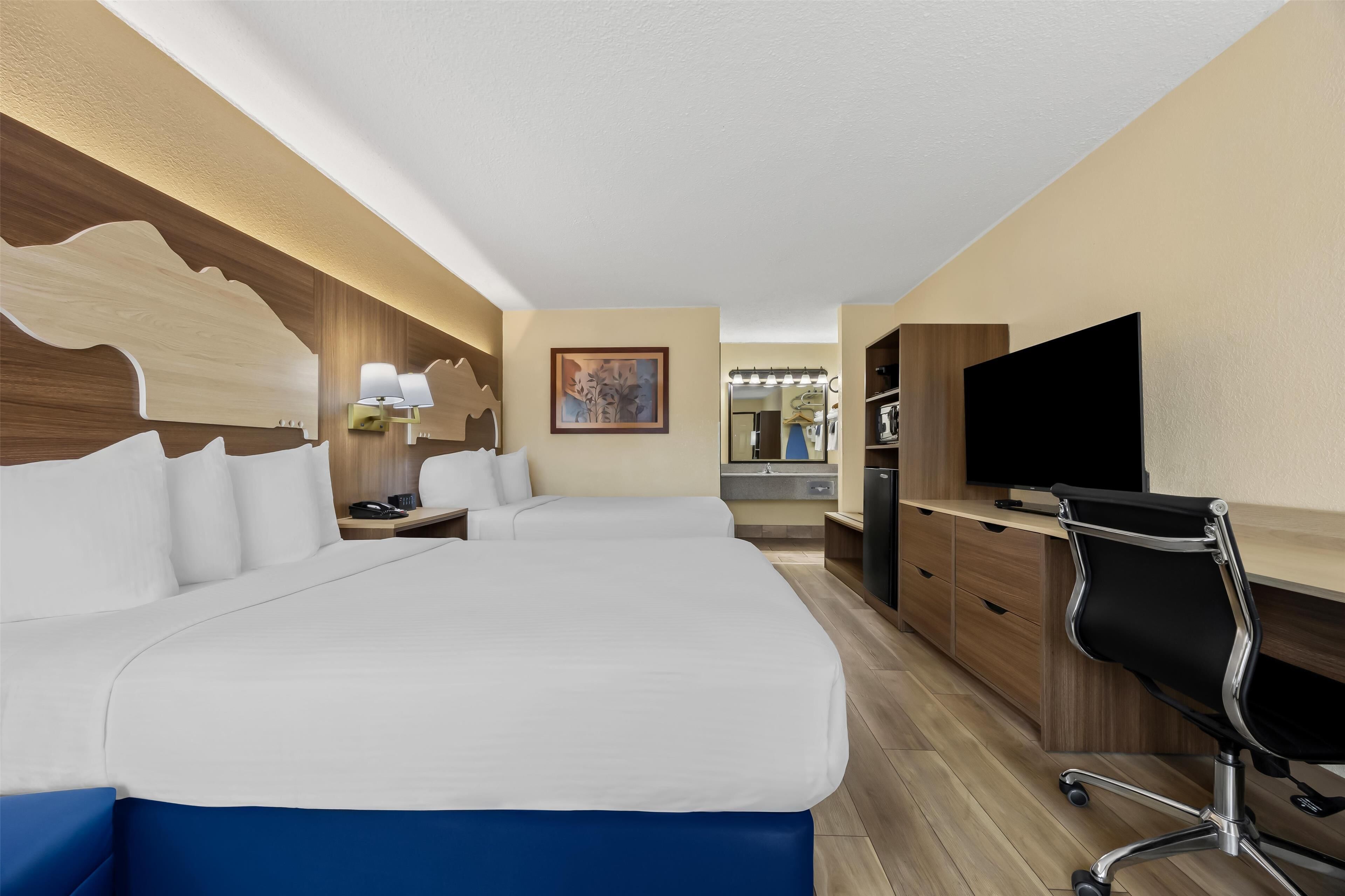 Habitación de hotel con dos camas, un escritorio con una silla, televisión y un baño a la vista.