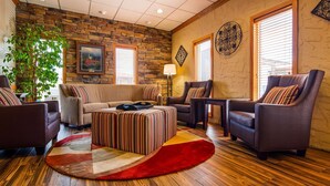 A cozy living room with a stone wall, a sofa, armchairs, a striped ottoman, and a red rug.