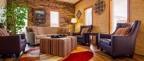 A cozy living room with a stone wall, a sofa, armchairs, a striped ottoman, and a red rug.