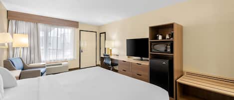 Hotellihuone, jossa on suuri sänky, työpöytä tuolilla, televisio, jääkaappi ja pieni oleskelualue, jossa on penkki.