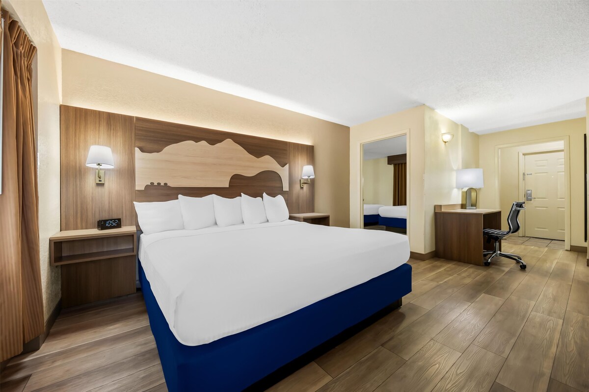 A hotel room with a large bed, wooden headboard, bedside lamps, a desk with a chair, and a mirror.