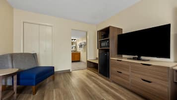 A compact living space with a kitchenette, a flat-screen TV, a blue bench, and a wooden dining table.