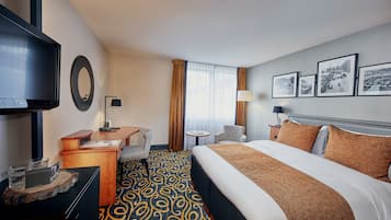 A hotel room with a bed, a desk, a television, a chair, a small table, and a window with curtains.