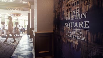 A hotel lobby with a large mural of a cityscape, a patterned floor, and a woman walking in the background.