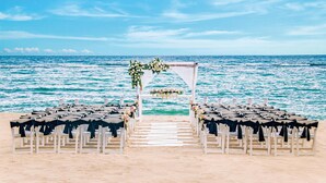 A beach wedding setup with white chairs and a floral arch. - Oasis Palm - All Inclusive (Cancun)