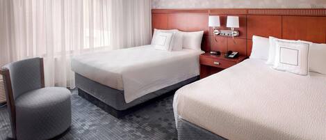 A hotel room with two beds, a chair, a nightstand with lamps, and a phone.
