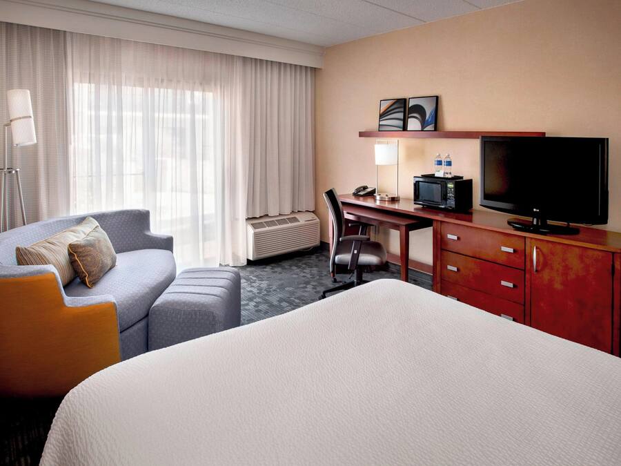Een hotelkamer met een groot bed, een bureau met een televisie, een stoel, een bank en een lamp.