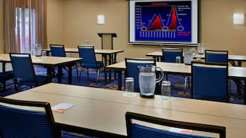 Un salón de conferencias con mesas, sillas y una pantalla que muestra un gráfico de la relación Dow/Gold.