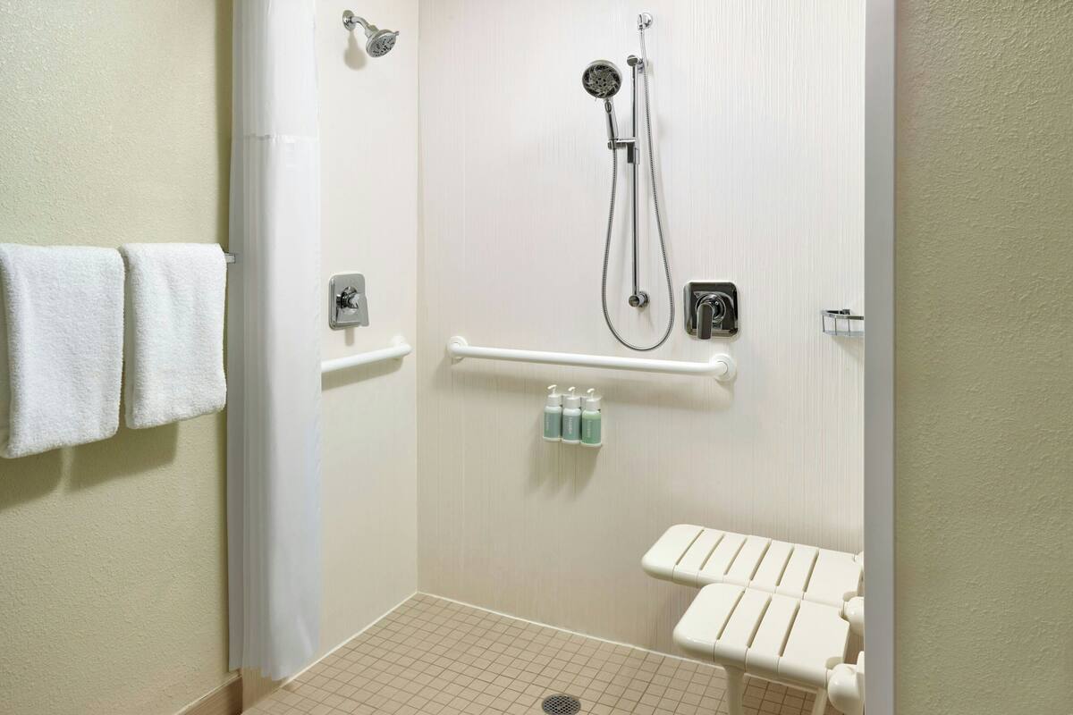 Un baño con ducha, barras de apoyo, inodoro y perchero para toallas.