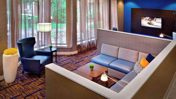 Een moderne hotelkamer met een bank, fauteuil en een televisie aan de muur.
