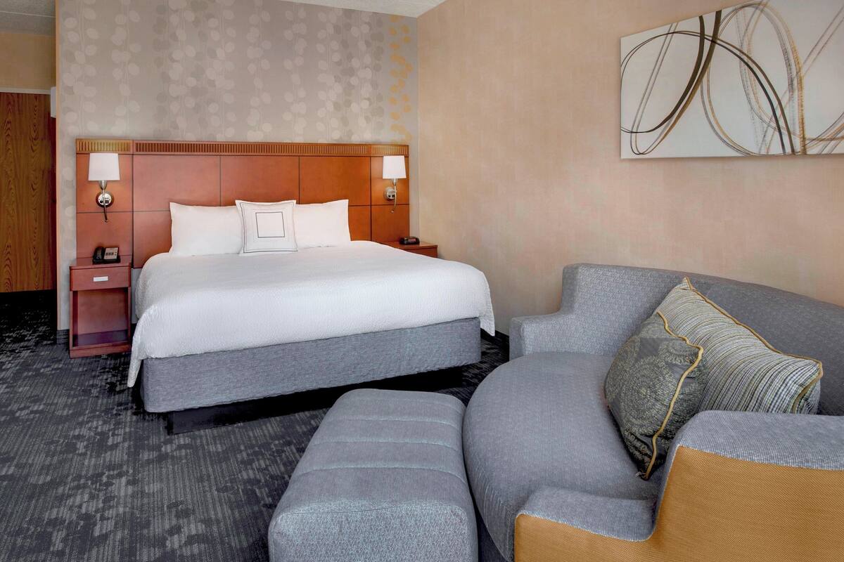 Habitación de hotel con una cama grande, dos mesitas de noche, un sofá y una obra de arte abstracta colgada en la pared.