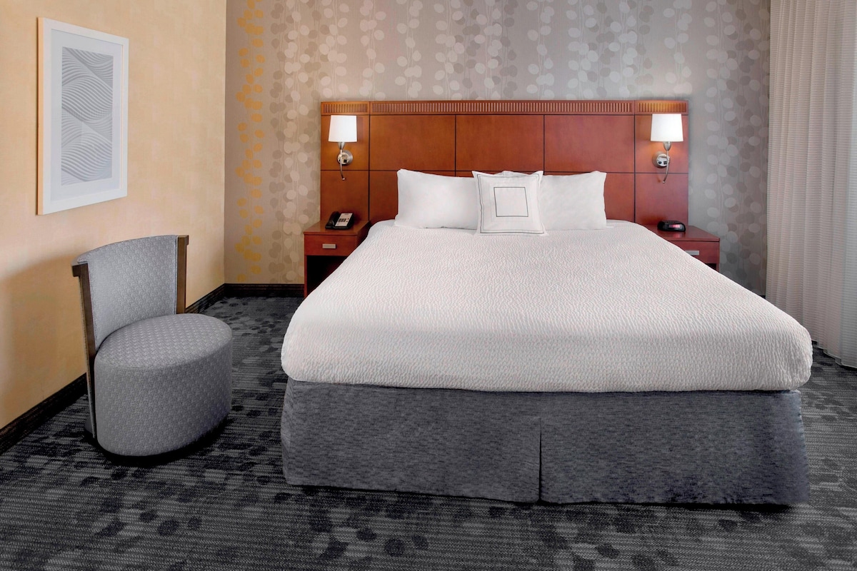 Ein Hotelzimmer mit einem großen Bett, einem Sessel, einem Nachttisch mit Telefon und einer Wandlampe.
