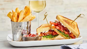 Un plato con un sándwich a la parrilla, una copa de vino blanco y una porción de papas fritas.
