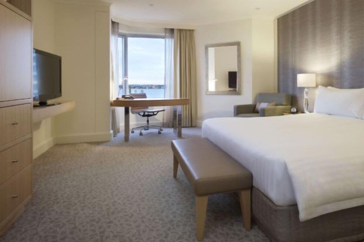 Ein Hotelzimmer mit einem großen Bett, einem Schreibtisch mit Stuhl, einem Fernseher und Blick ins Freie.