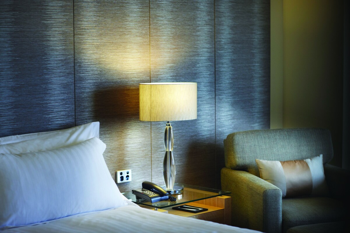 Ein Hotelzimmer mit einem Bett, einem Nachttisch mit Lampe, einem Telefon und einem Sessel.