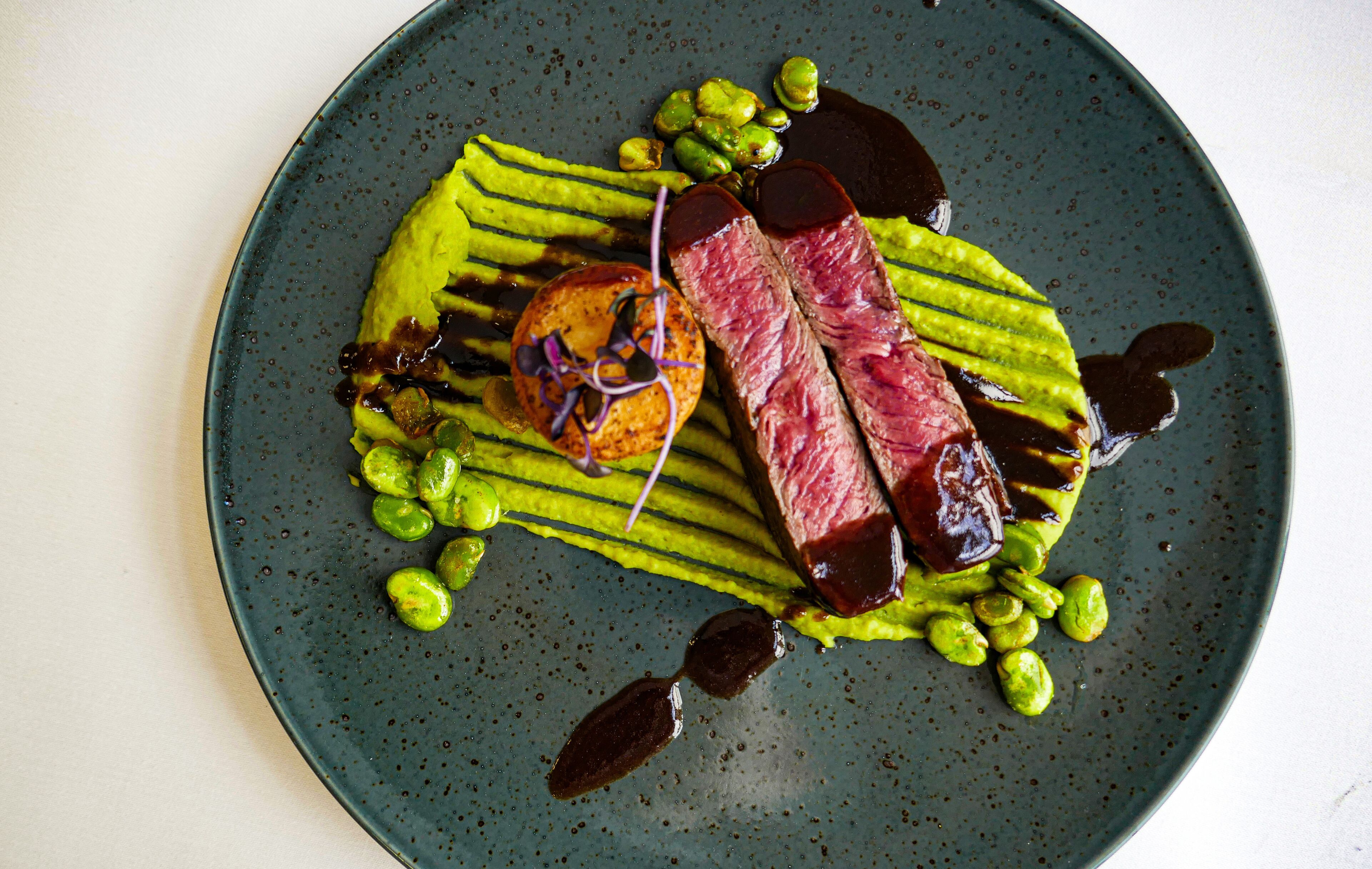 A plate with a steak, green sauce, and green vegetables.