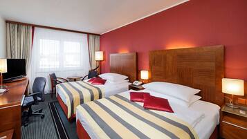 Ein Hotelzimmer mit zwei Betten, einem Schreibtisch, einem Fernseher und einem Sessel.