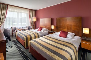Habitación de hotel con dos camas, un escritorio, una silla y un ventanal con cortinas.