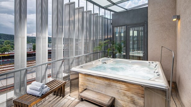 Ein Whirlpool auf einem Balkon mit einer hölzernen Sitzbank und Handtüchern, mit Blick auf eine Stadtlandschaft.