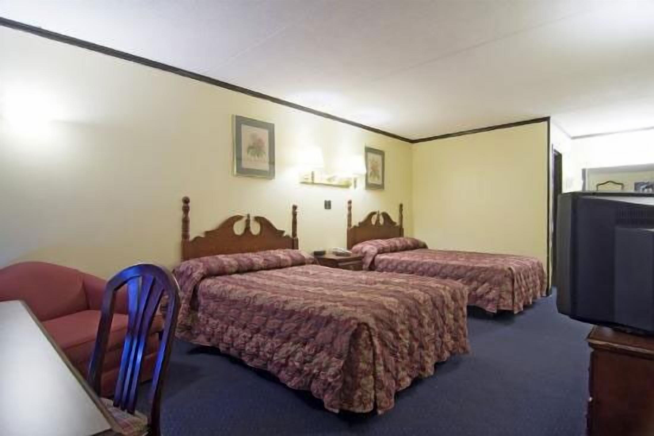 A hotel room with two beds, a chair, a desk, and a television.