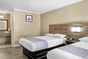 A hotel room with two beds, a wooden headboard, a bedside table with a phone, and a framed picture on the wall.