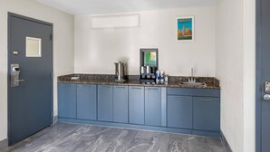Une cuisine moderne avec des meubles bleus, un plan de travail en granit, une machine à café et un tableau encadré au mur.