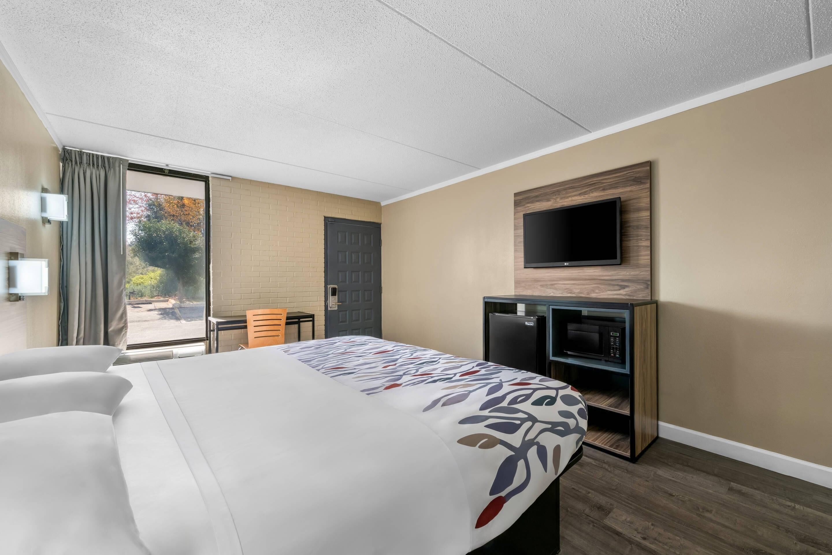 A hotel room with a bed, a desk, a television, and a sliding door to a balcony.