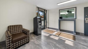 Un hall d’entrée avec un fauteuil à motifs, un distributeur automatique de billets, un comptoir d’accueil et une grande fenêtre.