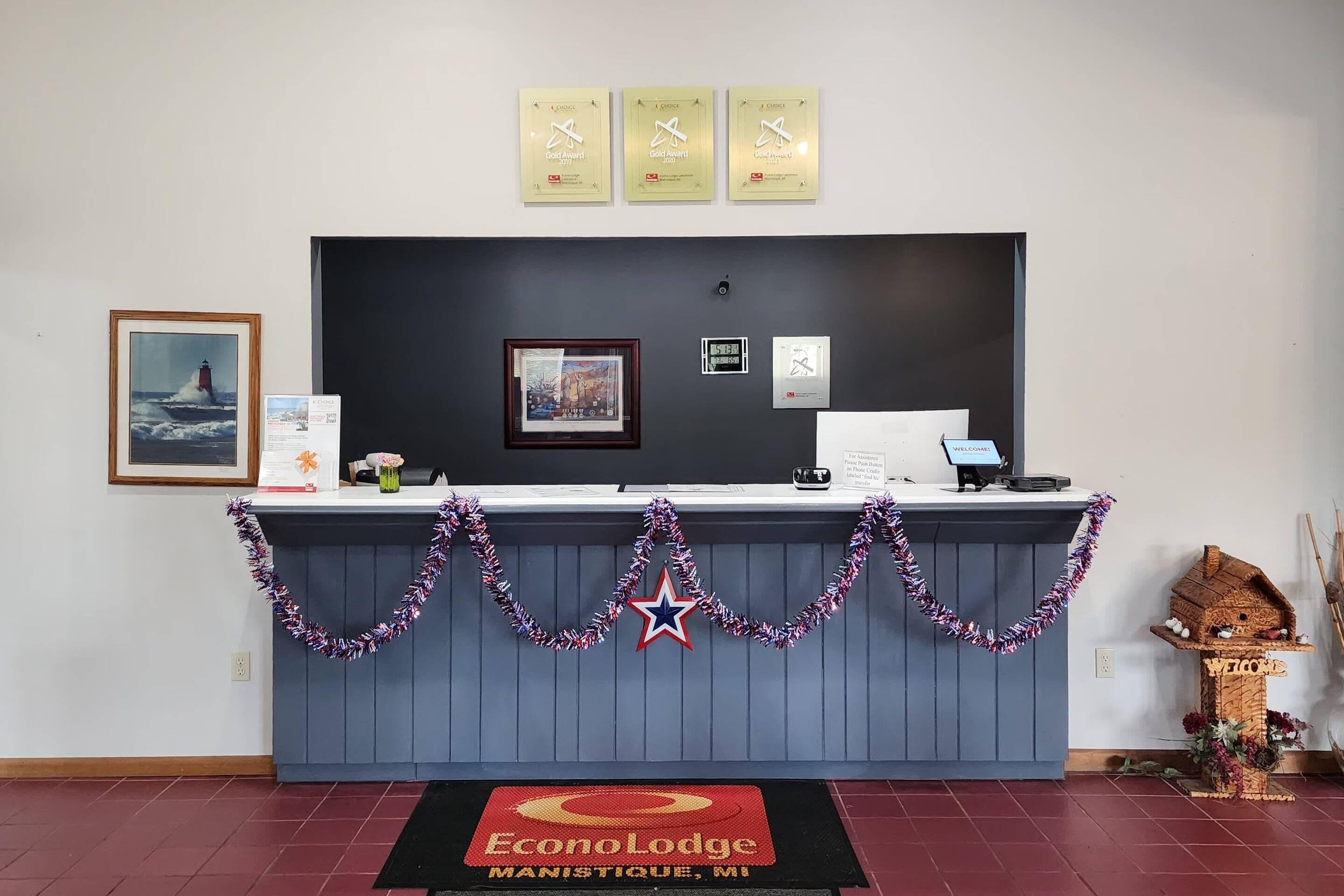 A reception desk with a framed painting, a clock, and three awards on the wall.