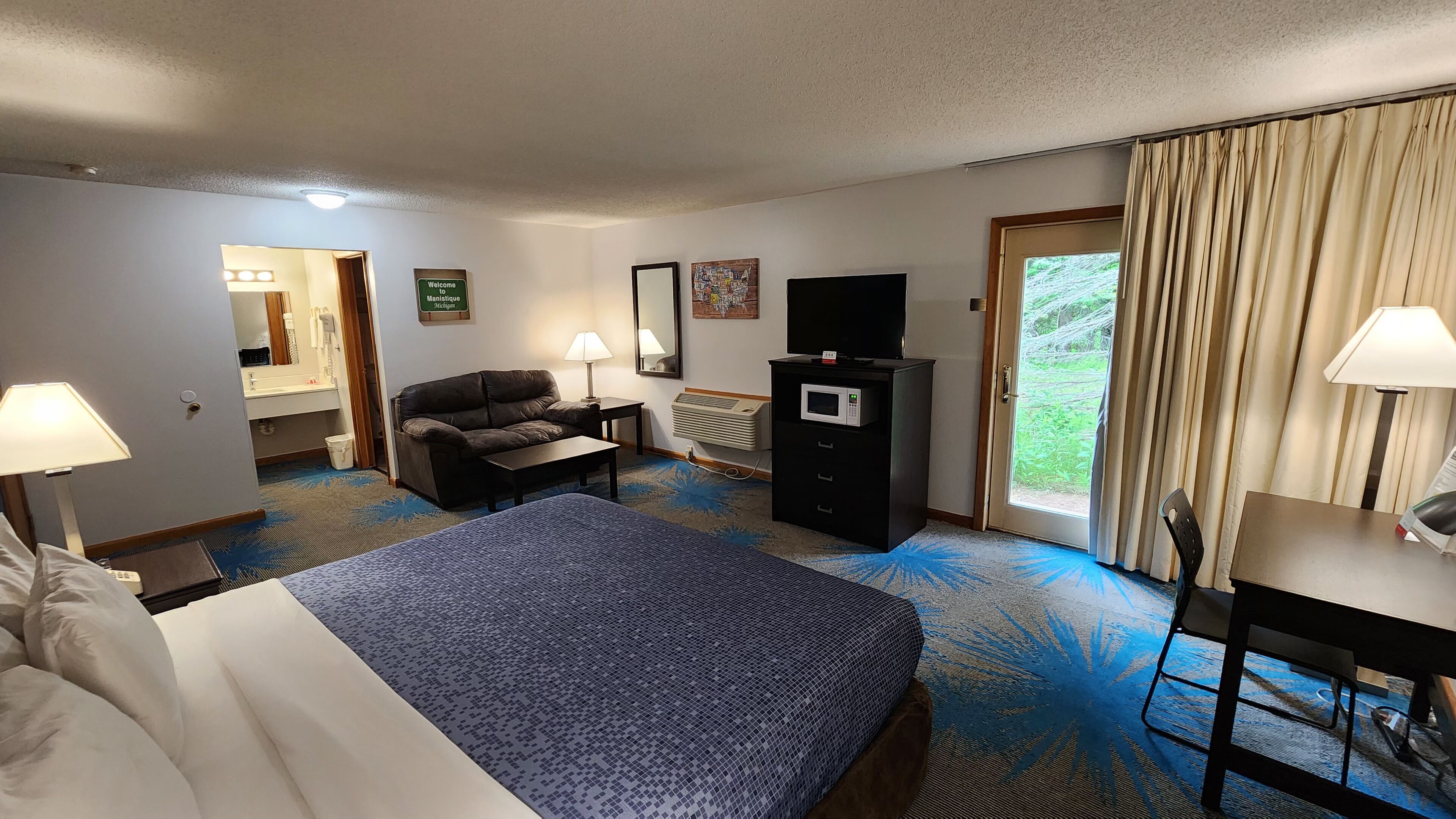 A hotel room with a bed, a sofa, a desk, a TV, and a window with curtains.