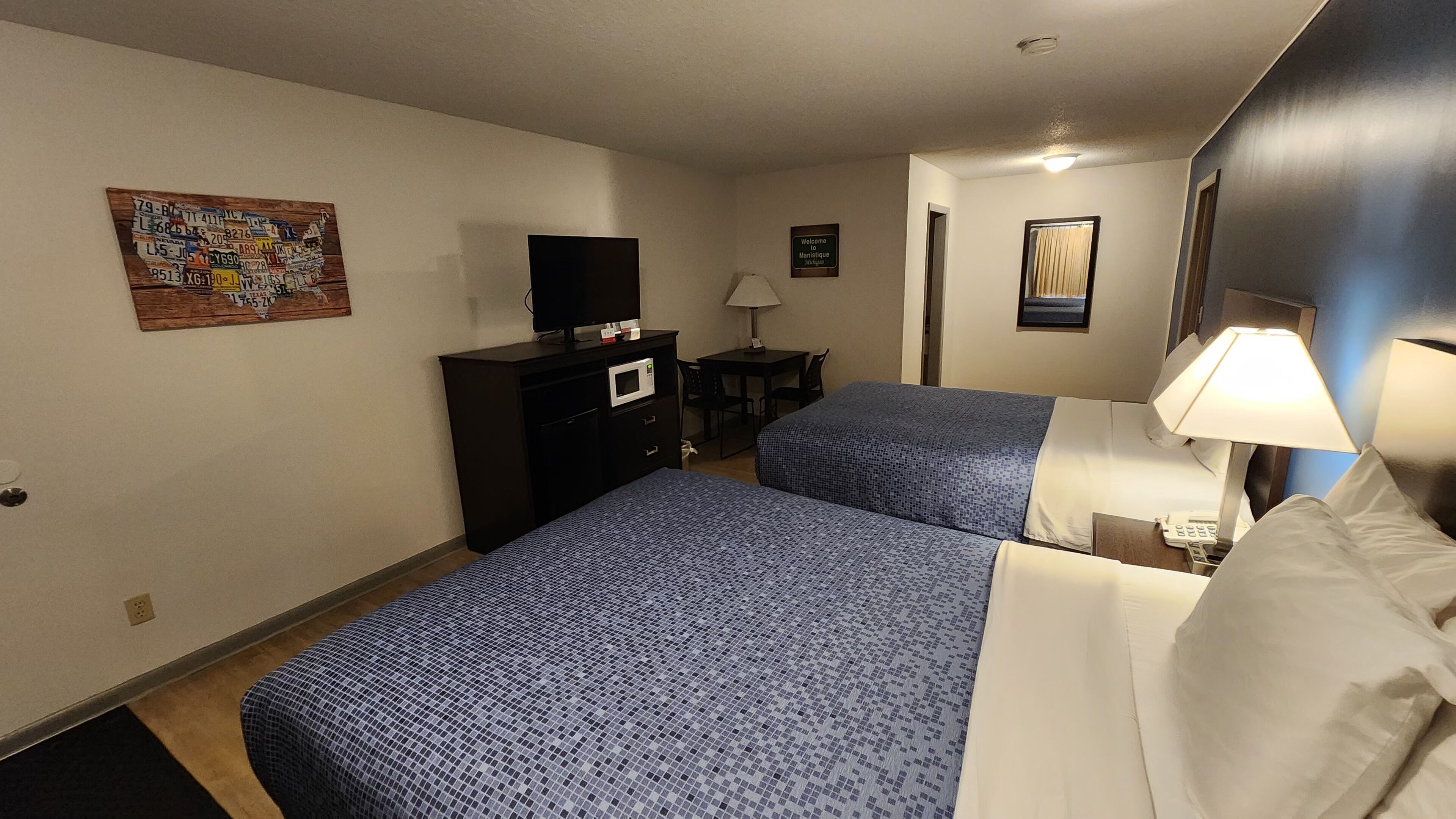 Een hotelkamer met twee bedden, een bureau, een televisie en een schilderij aan de muur.