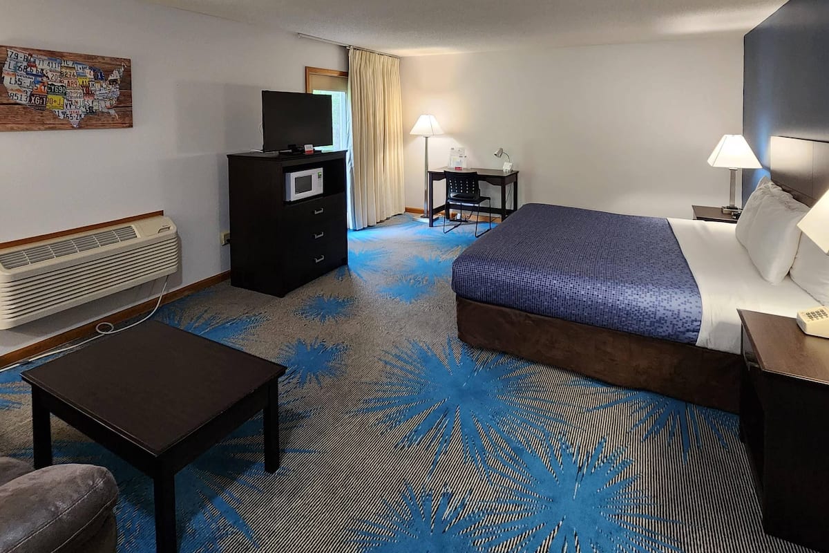A hotel room with a bed, a desk, a chair, a television, a desk lamp, a nightstand, and a wall-mounted air conditioner.